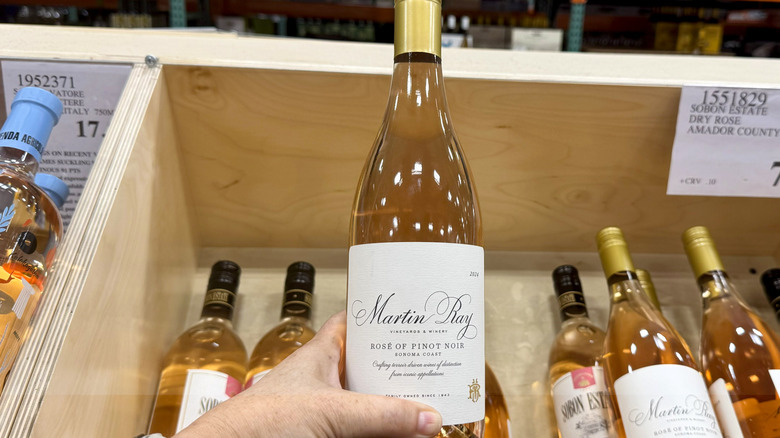 hand holding bottle of rose wine in front of wine crate