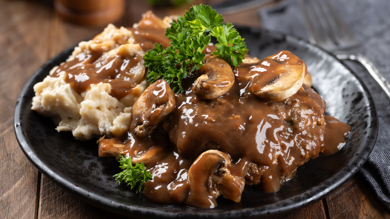 Salisbury Steak in a mushroom gravy with mashed potatoes on a black plate