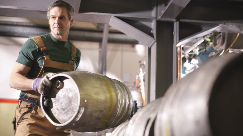A man in coveralls picking a keg up out of a stack