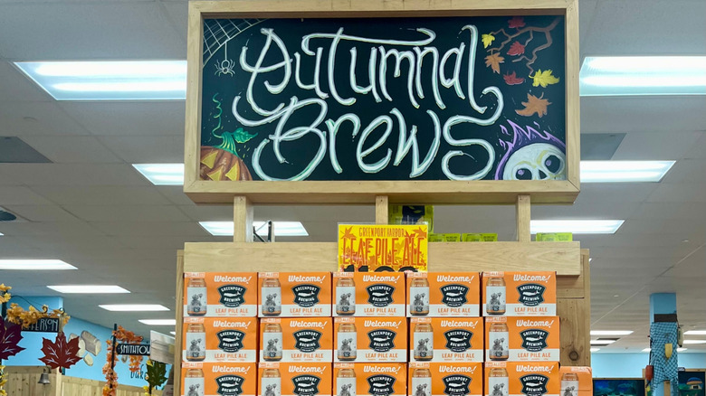 A Trader Joe's aisle display of orange beer cases with a board reading Autumnal Brews