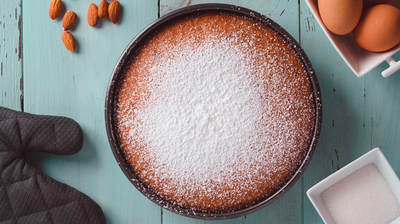 Homemade almond cake, with ingredients and an oven glove surrounding it