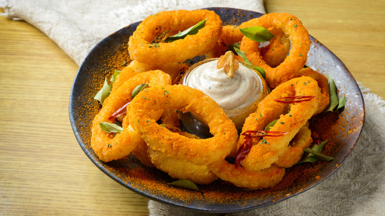 A plate of onion rings with a sour cream dip