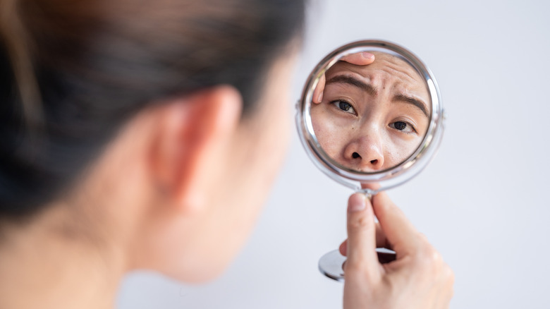 Woman looking into a mirror to examine acne