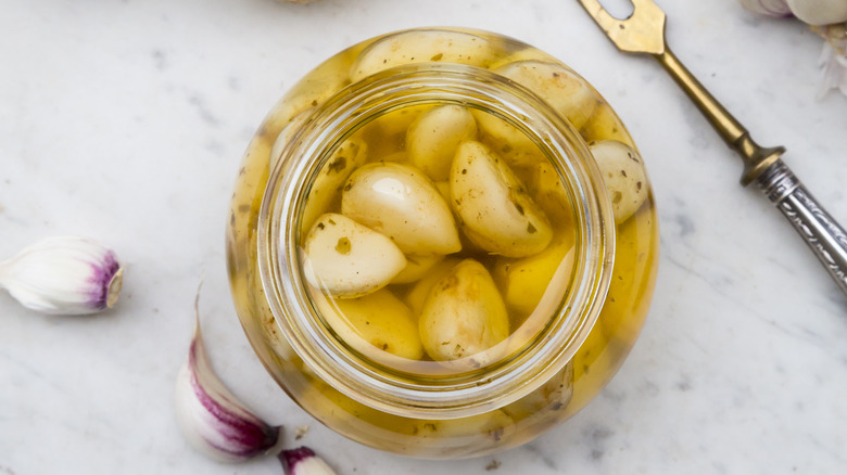 An open jar of oil with cloves of preserved garlic
