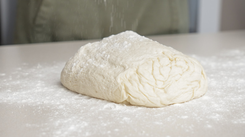 Properly proofed pizza dough sits on a flour-covered white surface