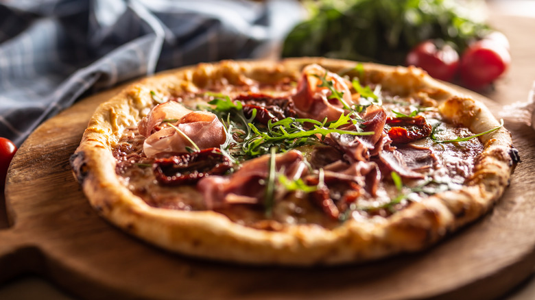 A homemade pizza with toppings sits on a wooden pizza tray