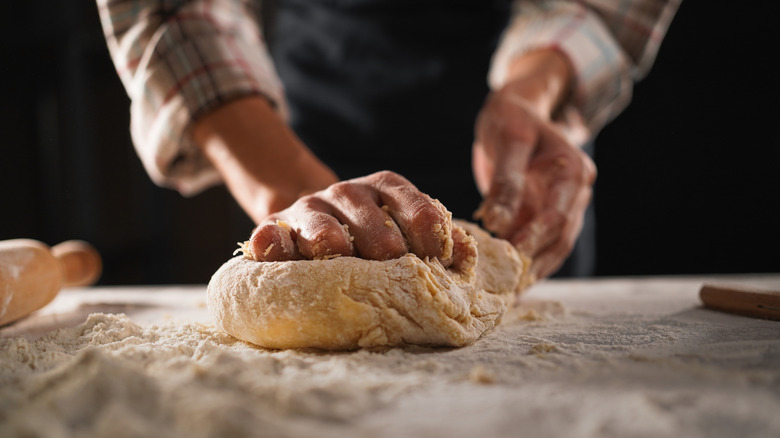 Hands kneading a ball of dough on a flour-covered surface