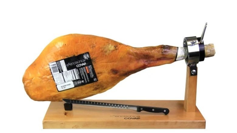 A person slicing of some ham from a ham leg