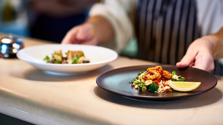 A chef places two dishes on the pass in a restaurant