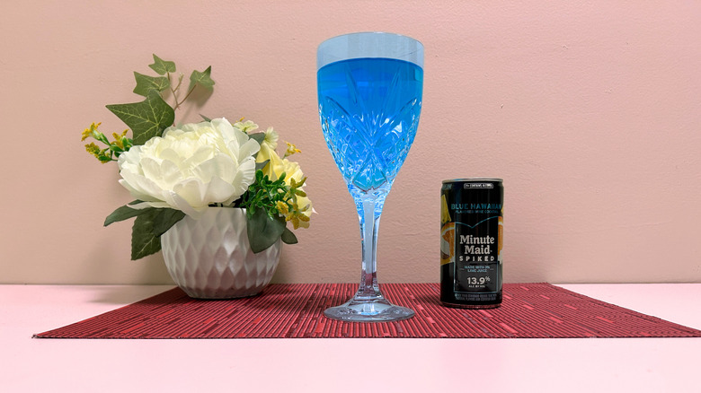 A can of Minute Maid Spiked Blue Hawaiian next to a glass of blue liquor against a pink background