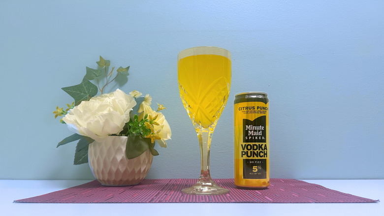 A can of Minute Maid Spiked Citrus Punch next to a glass of yellow liquor on a blue background