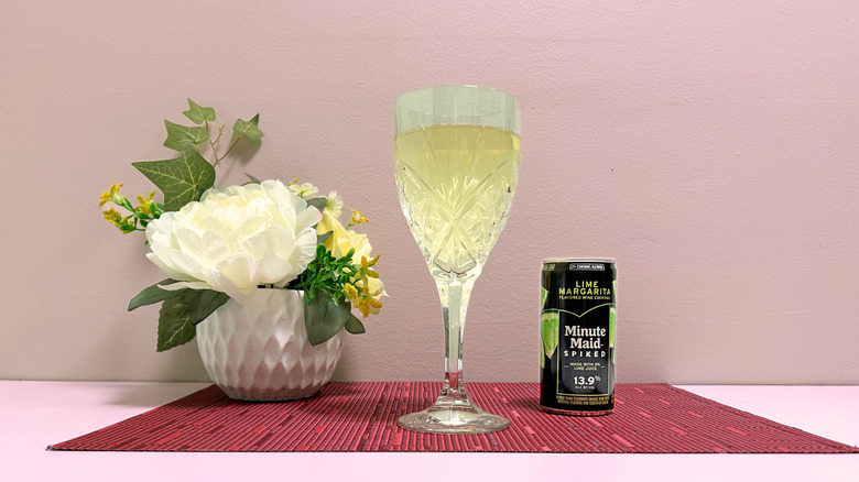 A can of Minute Maid Spiked Lime Margarita next to a glass of pale liquor on a pink background