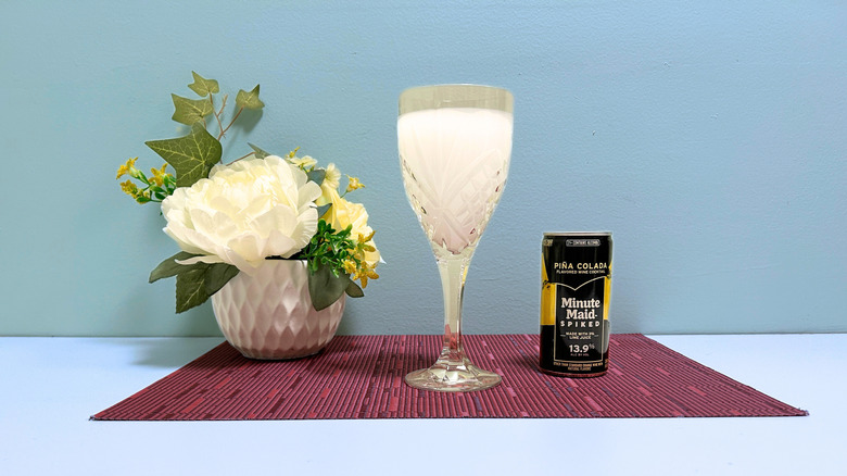 A can of Minute Maid Spiked Pina Colada next to a glass of white liquor against a blue background