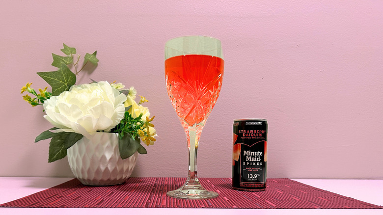 A can of Minute Maid Spiked Strawberry Daiquiri next to a glass of red liquor against a pink background