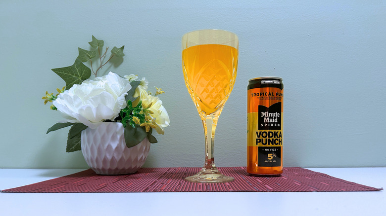 A can of Minute Maid Spiked Tropical Punch next to a glass of yellow liquor on a blue background