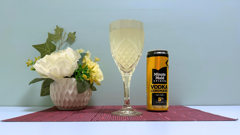 A can of Minute Maid Spiked Lemonade next to a glass of yellow liquor on a blue background