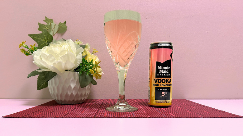 A can of Minute Maid Spiked Pink Lemonade next to a glass of pink liquor on a pink background