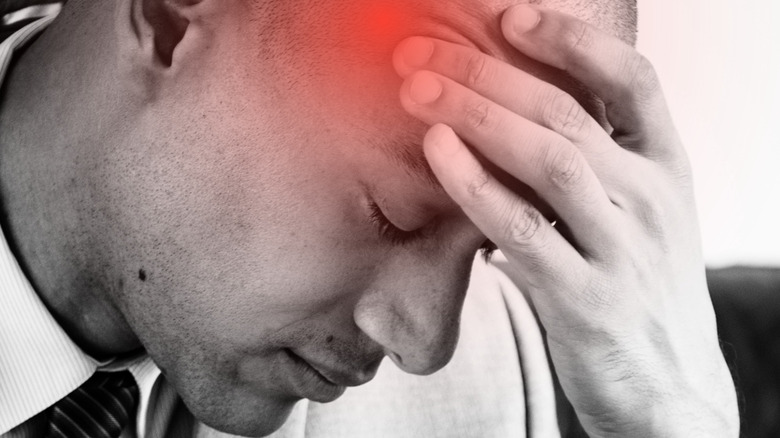 A man with his hand on his forehead with a red highlighted area suggesting a headache