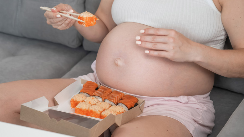 A pregnant woman eating rolls with chopsticks from a box