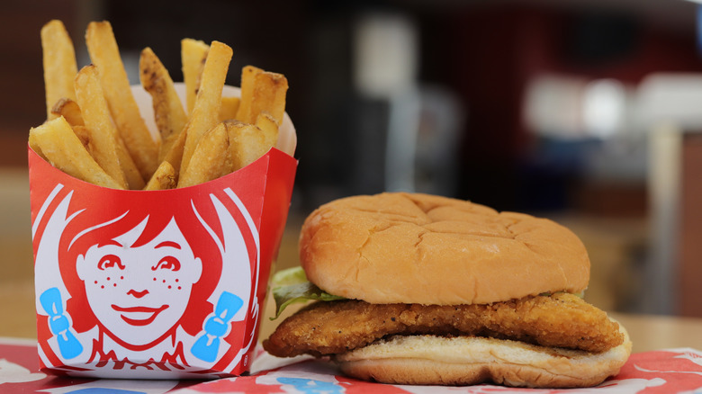 A chicken sandwich with only lettuce visible as a topping next to an order of Wendy's fries.