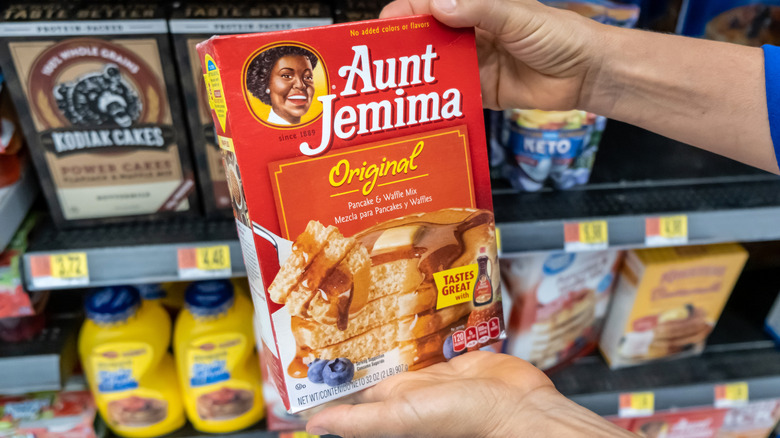 Hands holding a box of Aunt Jemima pancake mix in a grocery store.