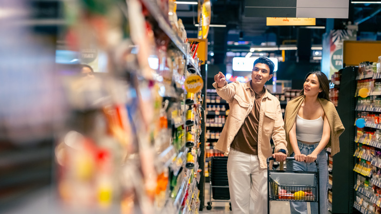 A couple with a shopping cart shopping in a grocery store.
