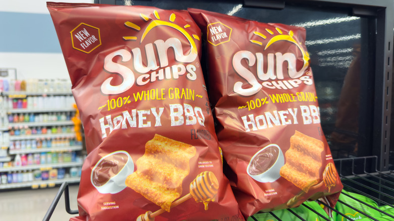 Two bags of Honey BBQ Sunchips on a wire rack shelf in the foreground, convenience store in the background.