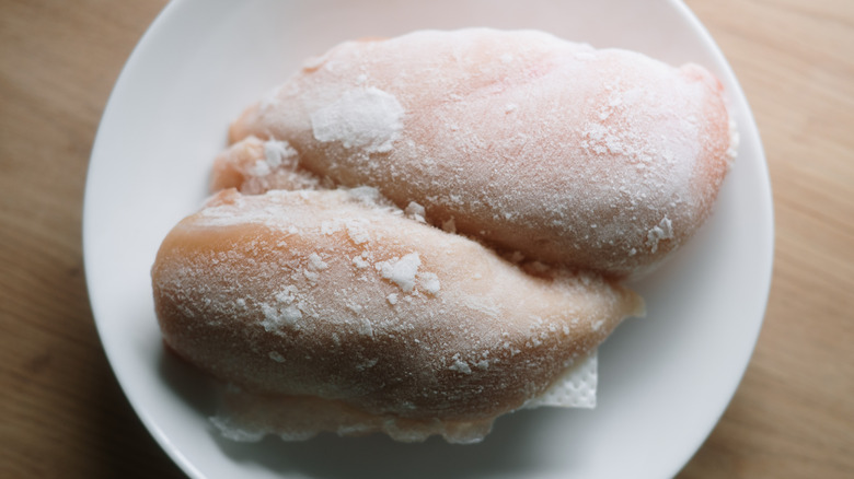Two frozen chicken breasts thawing on a plate