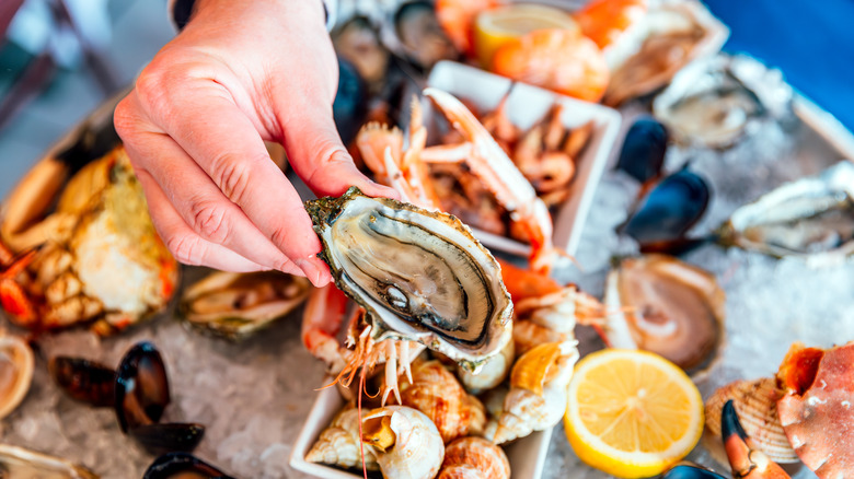 A man holding an oyster off a table with a variety of seafood on it