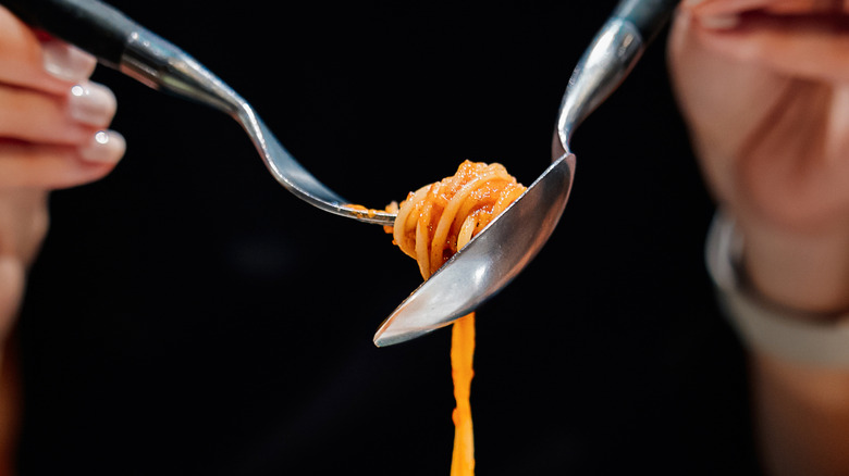 A person lifting spaghetti with a fork and spoon