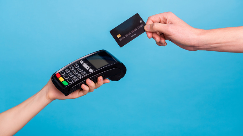A hand reaching to pay with a debit card on an electronic card machine