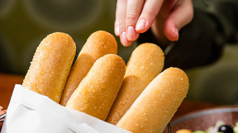 A hand reaching for some Olive Garden breadsticks