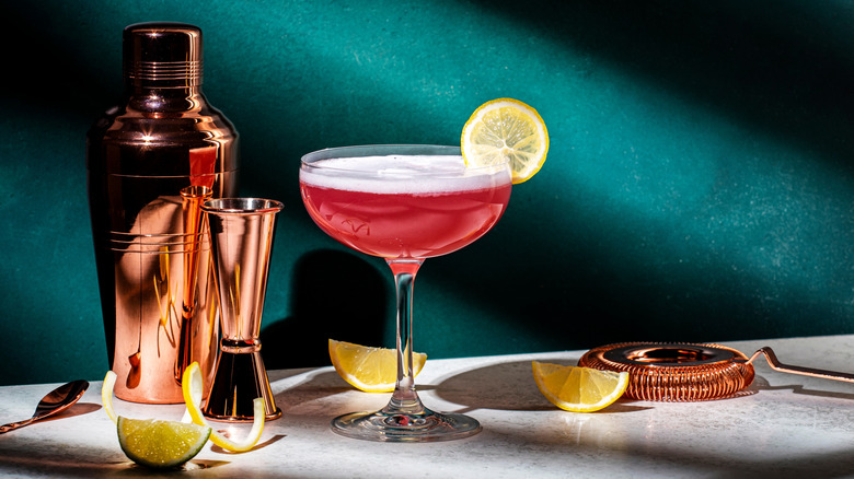 A Pink Lady cocktail sits next to cocktail equipment
