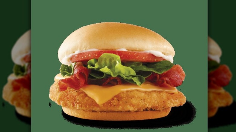 a Wendy's Crispy Chicken BLT, complete with fried chicken lettuce tomato bacon cheese and sauce, against a green background.