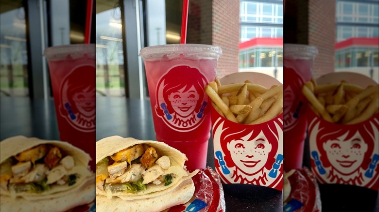 a grilled chicken Caesar wrap with Wendy's fries and drink next to it on a table.