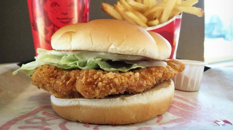 a Wendy's Spicy Chicken Sandwich on a table with fries, drink, and a ramekin of sauce.