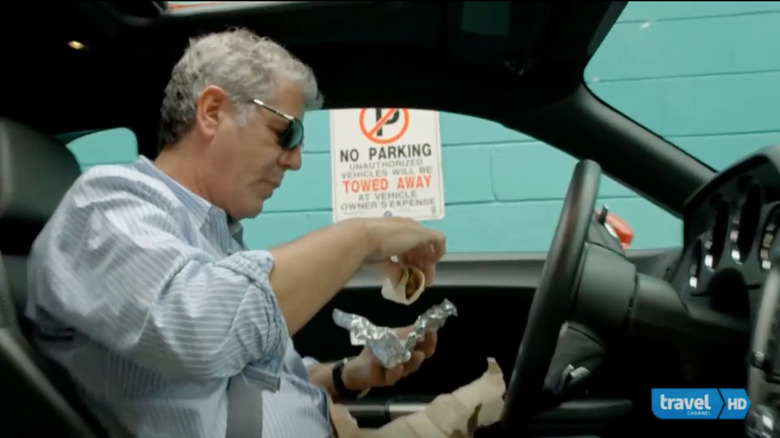 Anthony Bourdain eats a taco in his car.