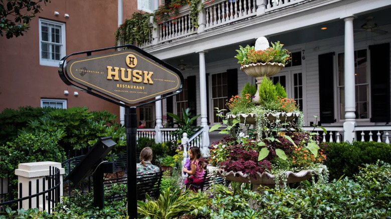 An exterior shot of Husk with a lush garden and fountain in front of a white restaurant with a large porch.