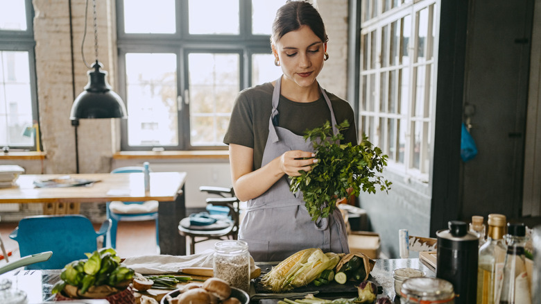 A woman cooking at home, holding a bunch of fresh parsley