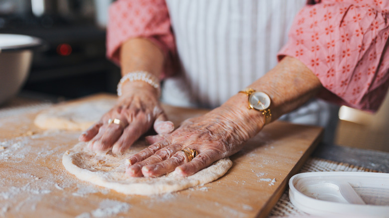 An old woman's hands spreading dough on a cutting board