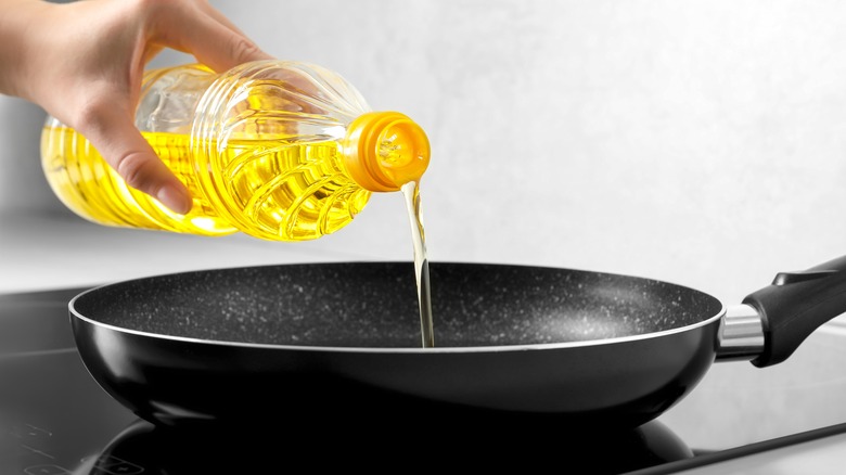 hand pouring oil into a frying pan