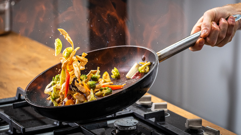 A man sauteeing fresh vegetables in a wok