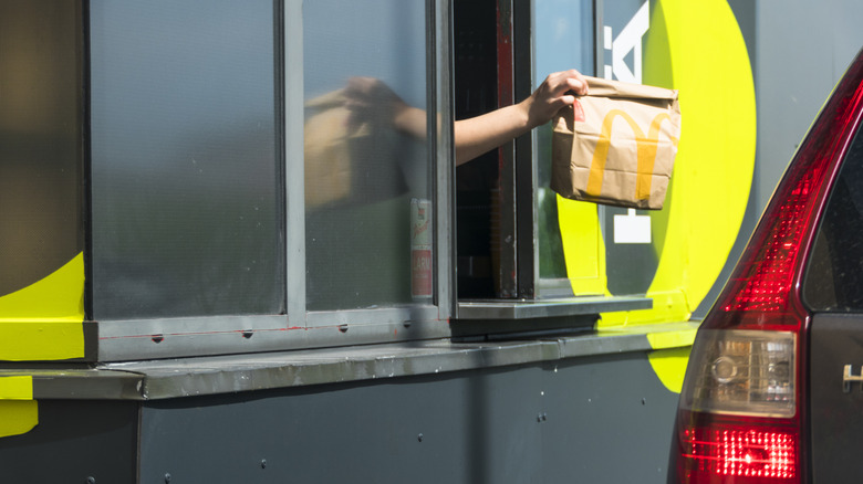 McDondald's employee handing bag of food through drive-thru window