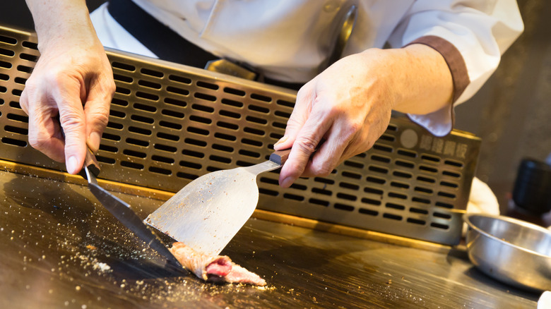 A chef using two spatulas to cook a slice of beef on the grill