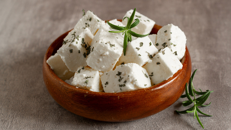Cubed feta in a bowl with dried basil and fresh rosemary