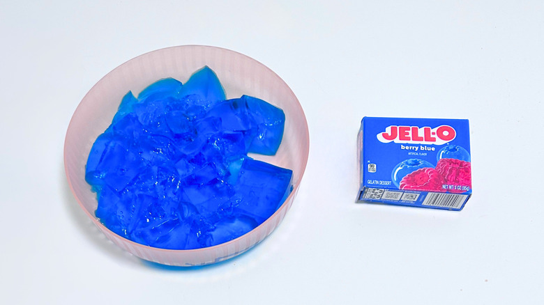A bowl of gelatin next to a packet of Jell-O Berry Blue