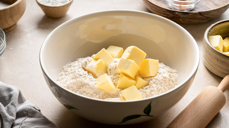 Butter and flour together in a bowl on a kitchen counter beside ingredient dishes and rolling pin