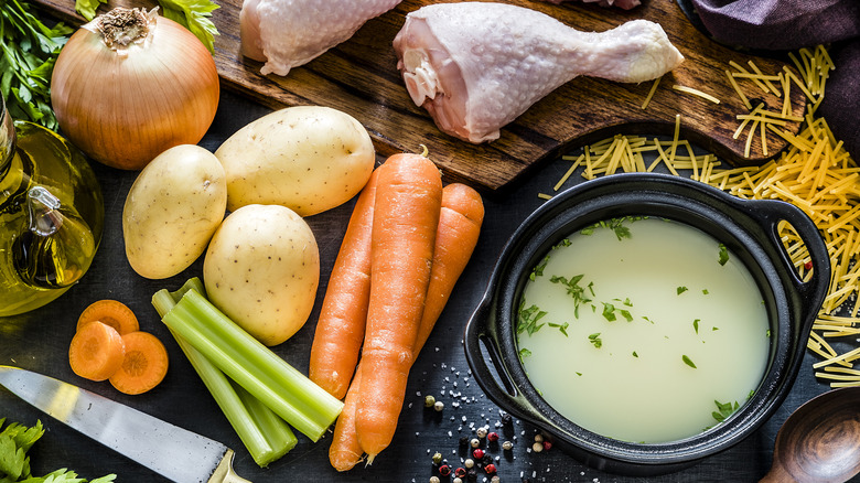 Pot of broth beside raw chicken, onion, potatoes, carrots, and celery