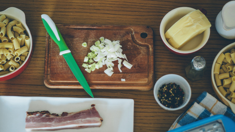 Uncooked pasta, raw bacon, spices, butter, and onion on a wooden surface