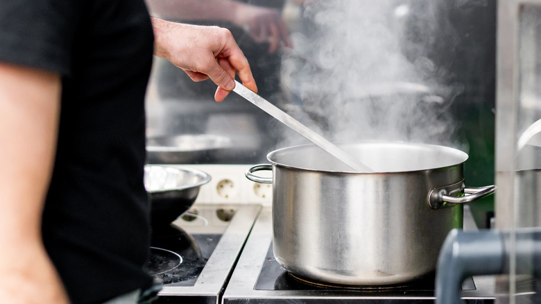 Person stirs a pot of hot soup on a stove